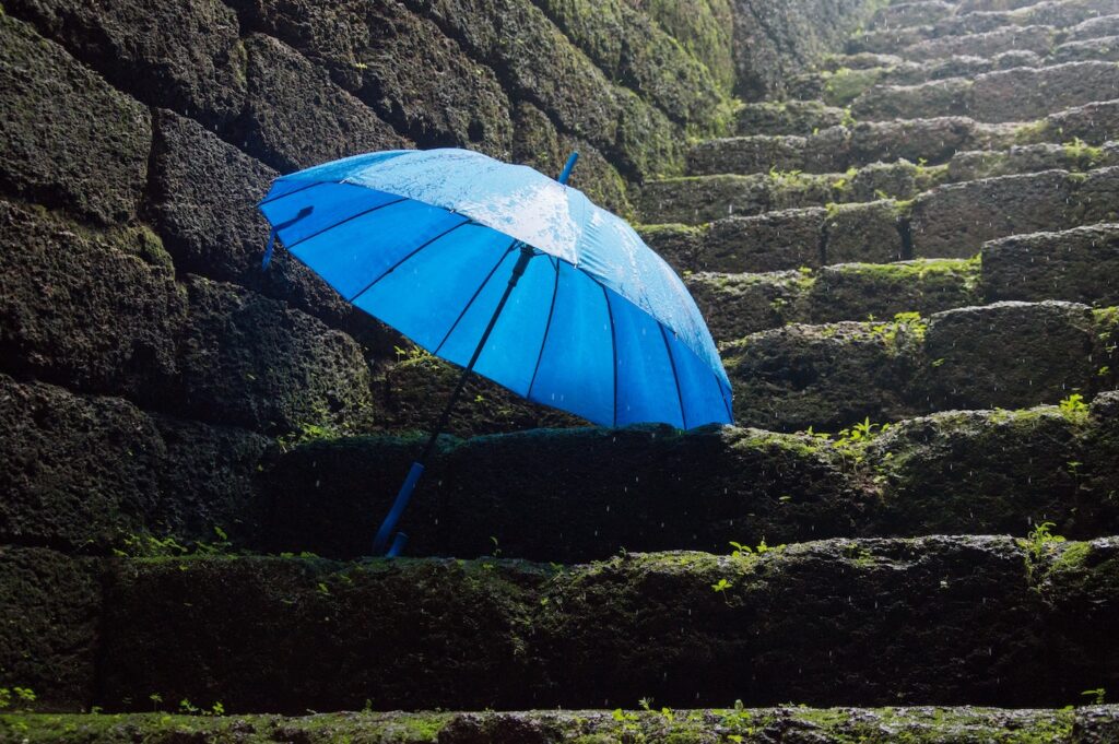 A bright blue umbrella is sitting upon a set of uneven stairs. There is a brick wall to the left of the umbrella, and the steps are also made of brick.