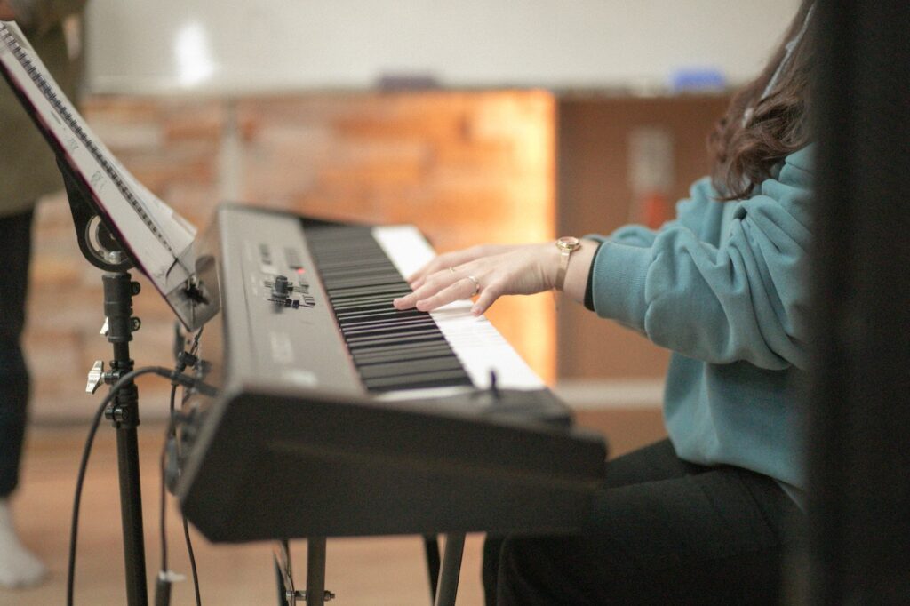 A woman sits at a piano playing a song. There is a stand with sheet music on it in front iof her.