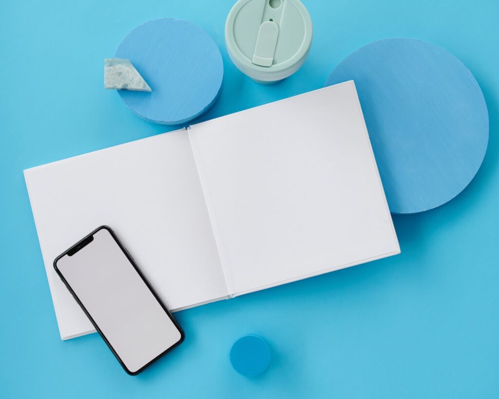 A white notebook with an iphone in a black case sit on top of a bright blue background.