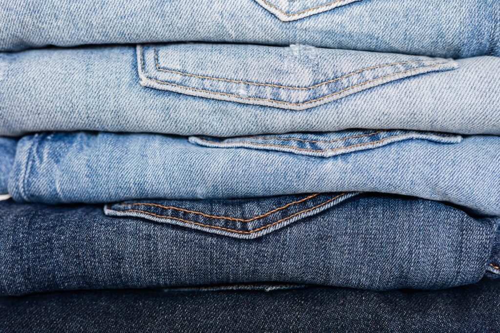 A stack of folded denim jeans, each with the pocket facing the front. They are neatly stacked in a gradient pattern from light to dark blue jeans.