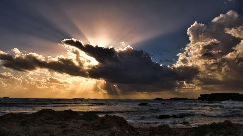 A group of dark clouds form in front of a sunset, with a wide ocean beneath.