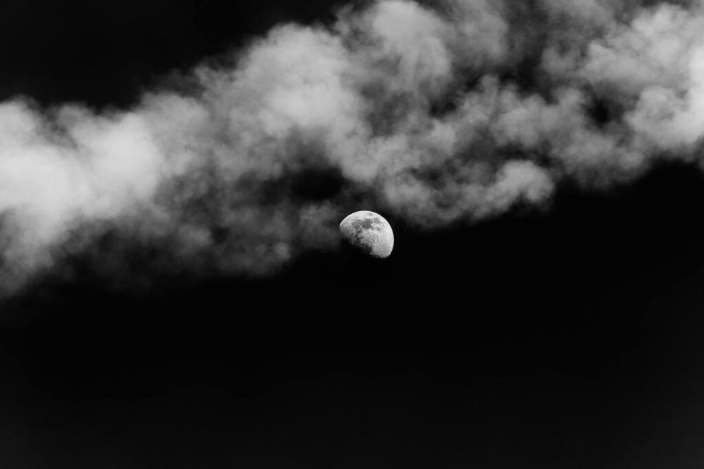 In the middle of a cloudy night sky sits the moon and a bunck of stars.