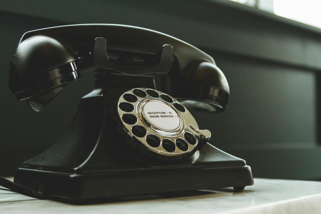 A close up photo of a rotary telephone sitting on a desk.